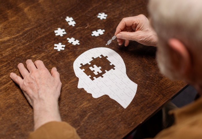 An elderly person doing a jigsaw puzzle shaped like a human head in profile