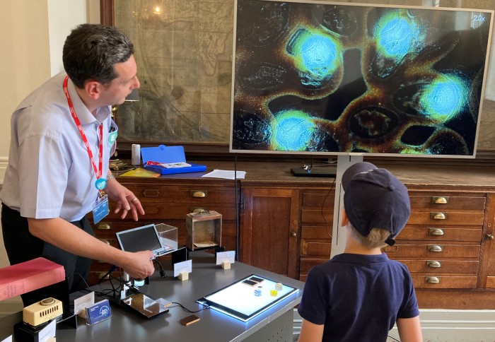 Professor Ambrose Taylor showing a young visitor what oriental lacquer with sprinkled gold decoration (maki-e) looks like close up through an optical microscope.