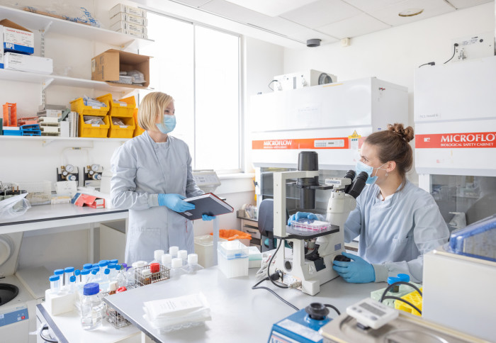 two women in lab wearing lab coats and face masks