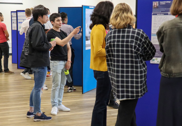 People standing near poster boards discussing the research posters that are pinned up