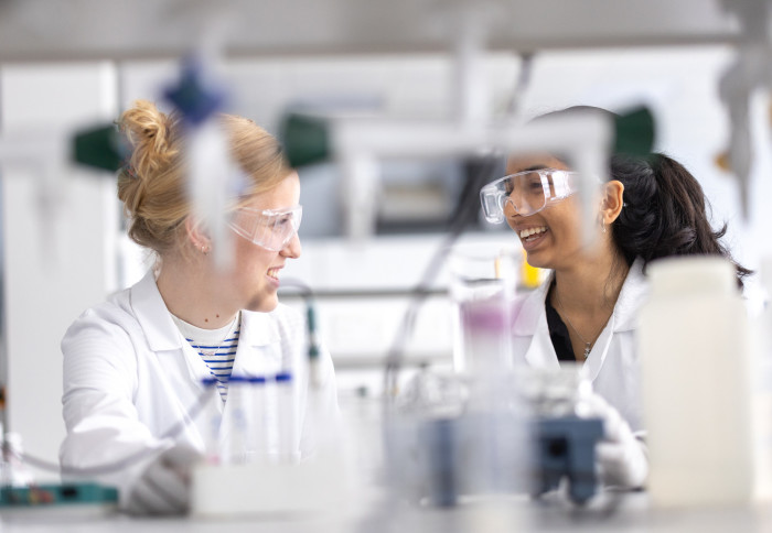 Two female students sitting at a laboratory bench, smiling and talking