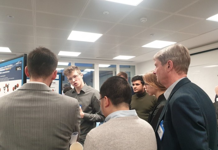 Alexander Thebelt presents an early-stage poster version of his NeurIPS 2022 paper at an internal Imperial workshop in 2019. Industrialists and researchers are standing around him, giving feedback.