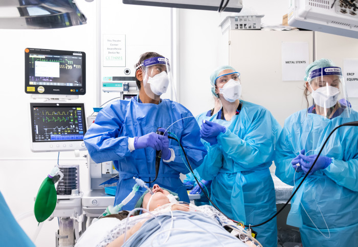 Patient lies in bed receiving treatment at a London hospital from medical team