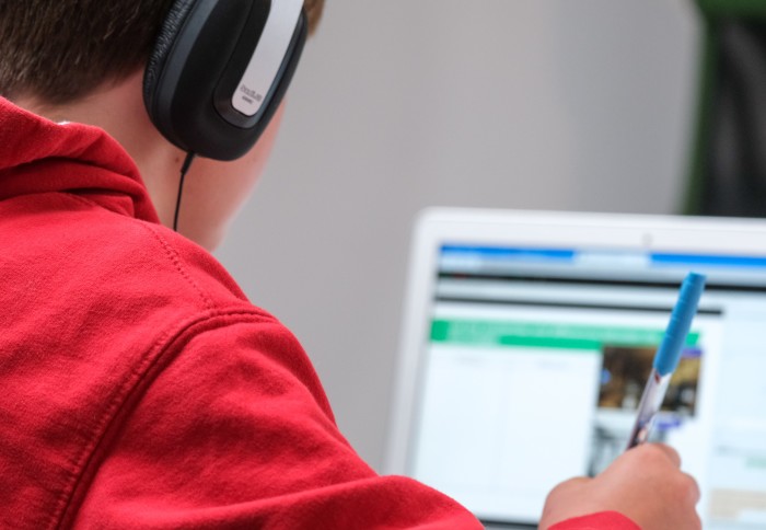 Person holding a pen and wearing headphones looking at a blurred laptop screen