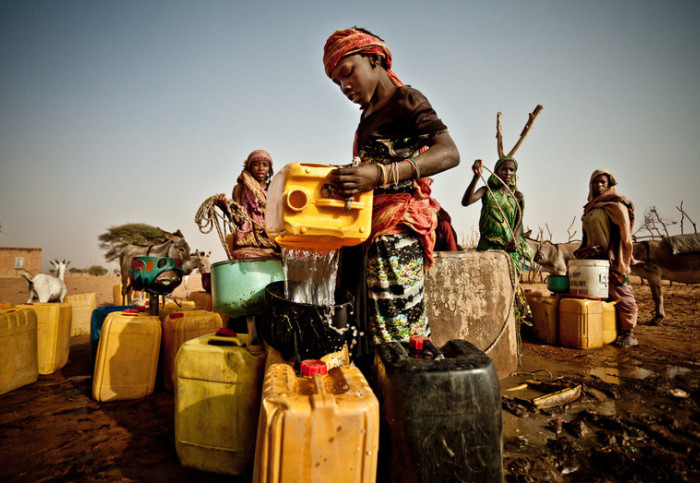 Mauritanian woman draws water from a well into a series of dirty plastic containers