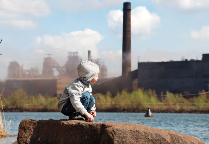 Playing little boy on the river coast in front of metallurgy plant
