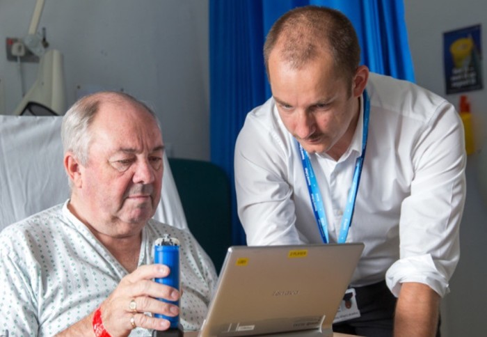 Patient sits in bed and looks at a screen with a healthcare professional