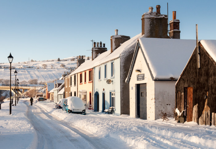 Helmsdale, Scotland, UK - December 2, 2010: A person walks their dog through winter snow on Shore Street in the village of Helmsdale in the Highlands of Scotland.