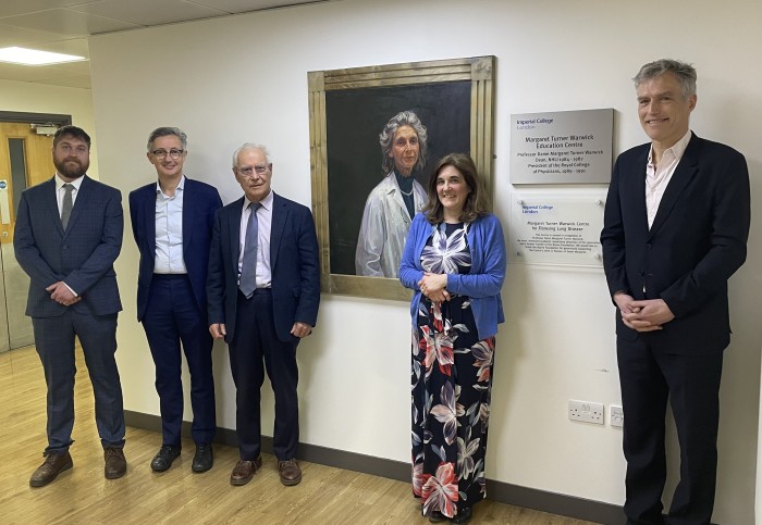 A group of people stand in front of a painting of Professor Dame Margaret Turner Warwick and plaques