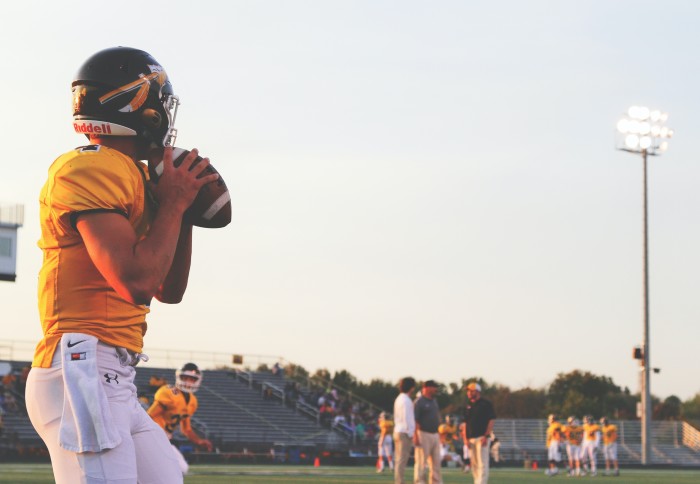 Picture of an man in an American football helmet and with an american football ready to throw it across the pitch.