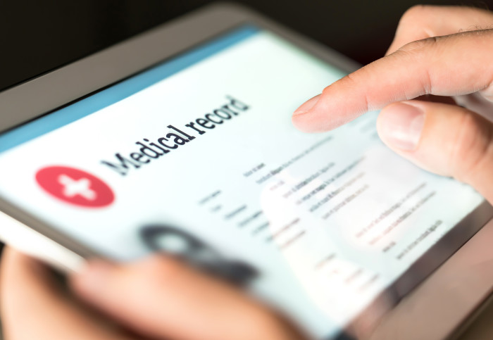 A photo of a person's hands, holding a tablet and scrolling a screen that says "Medical record"