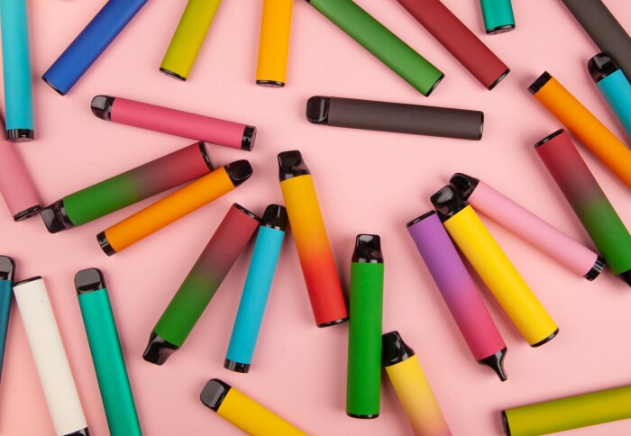 A collection of disposable e-cigarettes on a pink background.
