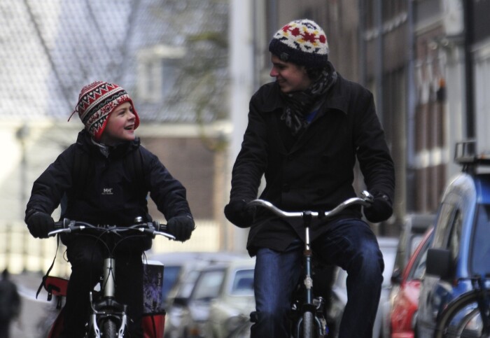 An adult and a child enjoying cycling through a street.