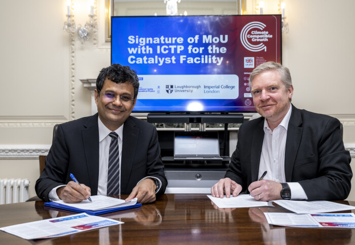Atish Dabholkar (left) and Mark Howells (right) sitting at a table with pens in hand, signing a document.