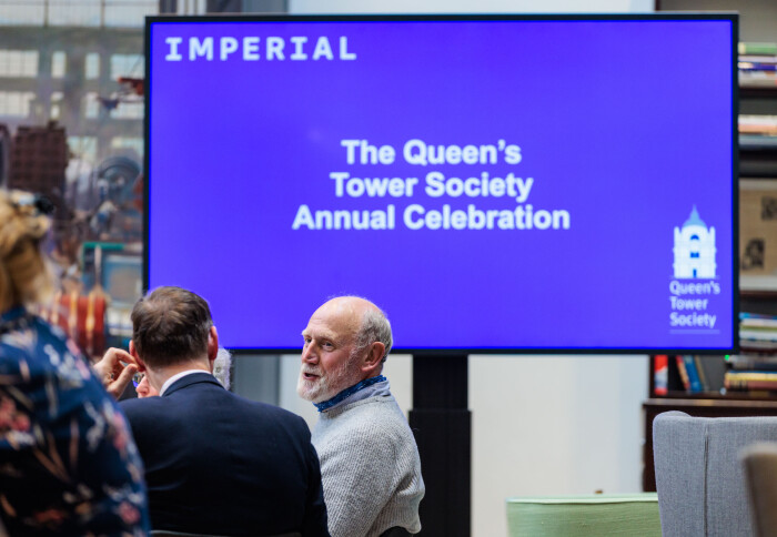 Two men speaking in front of screen that says 'The Queen's Tower Society Annual Celebration'