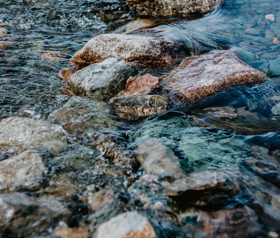 Photo of water running over rocks in the shallow area of a river. By pure-julia on Unsplash
