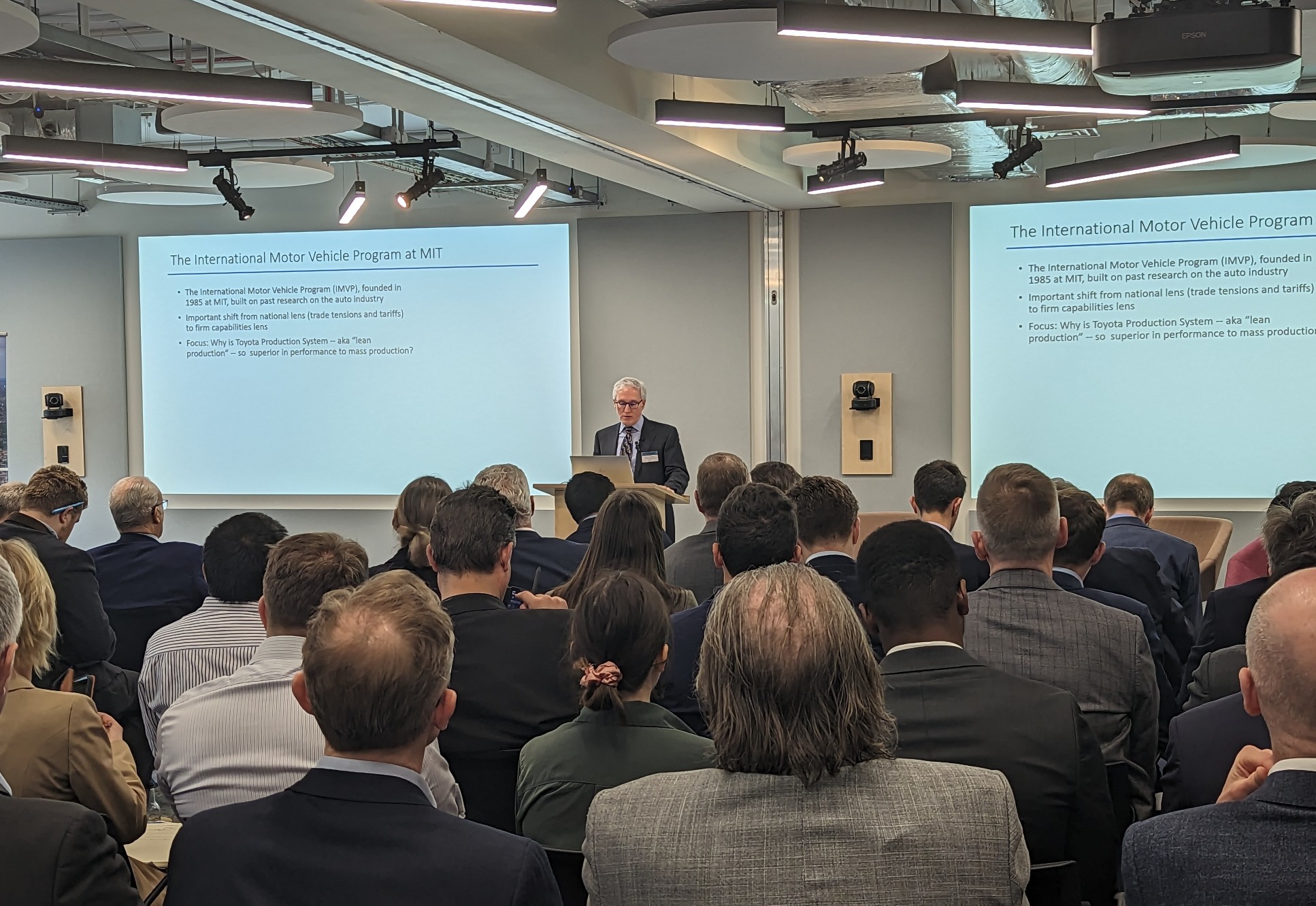 Professor John Paul MacDuffie speaking at a lectern in front of presentation slides at Innovation and Growth conference