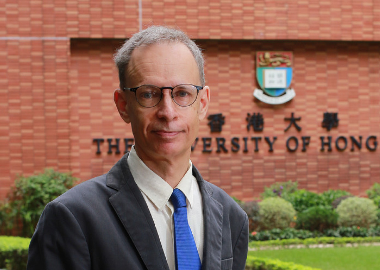 Man in suit and blue tie standing outside University of Hong Kong sign