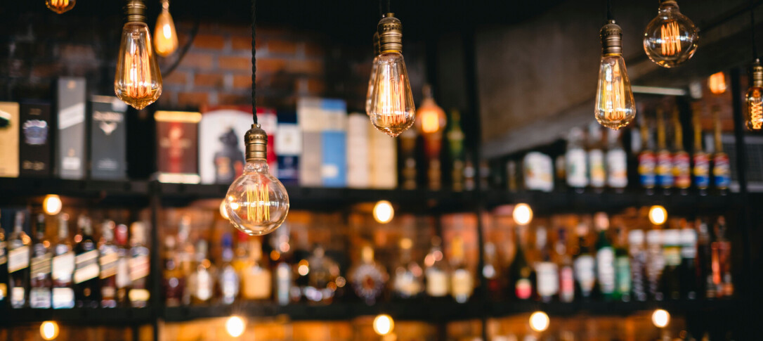 A blurred photo of a bar lit with lights showing drinks and lamps hanging from the ceiling