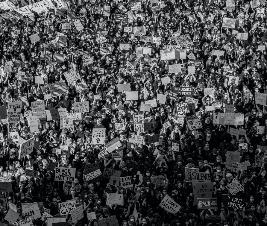 A black and white aerial image of a crowdof people, some with placards,  during a Black Lives Matter protest. 