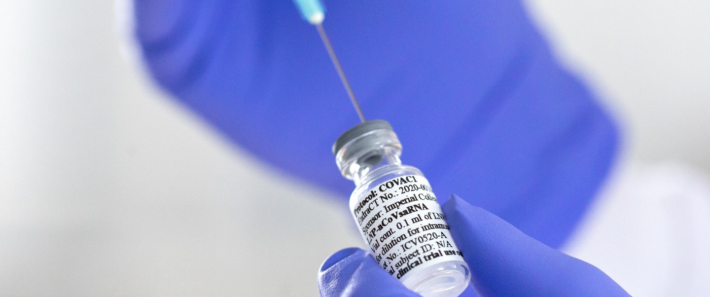 A gloved hand using a syringe to draw out COVID vaccine