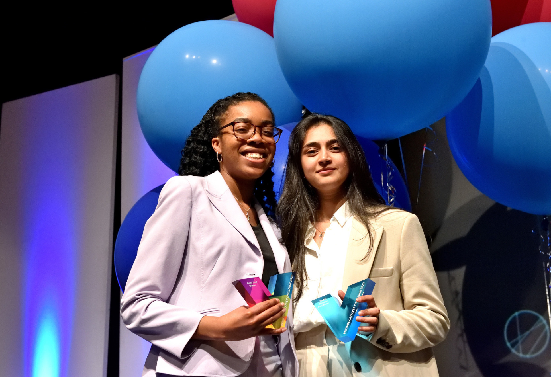 Two women smile holding trophies