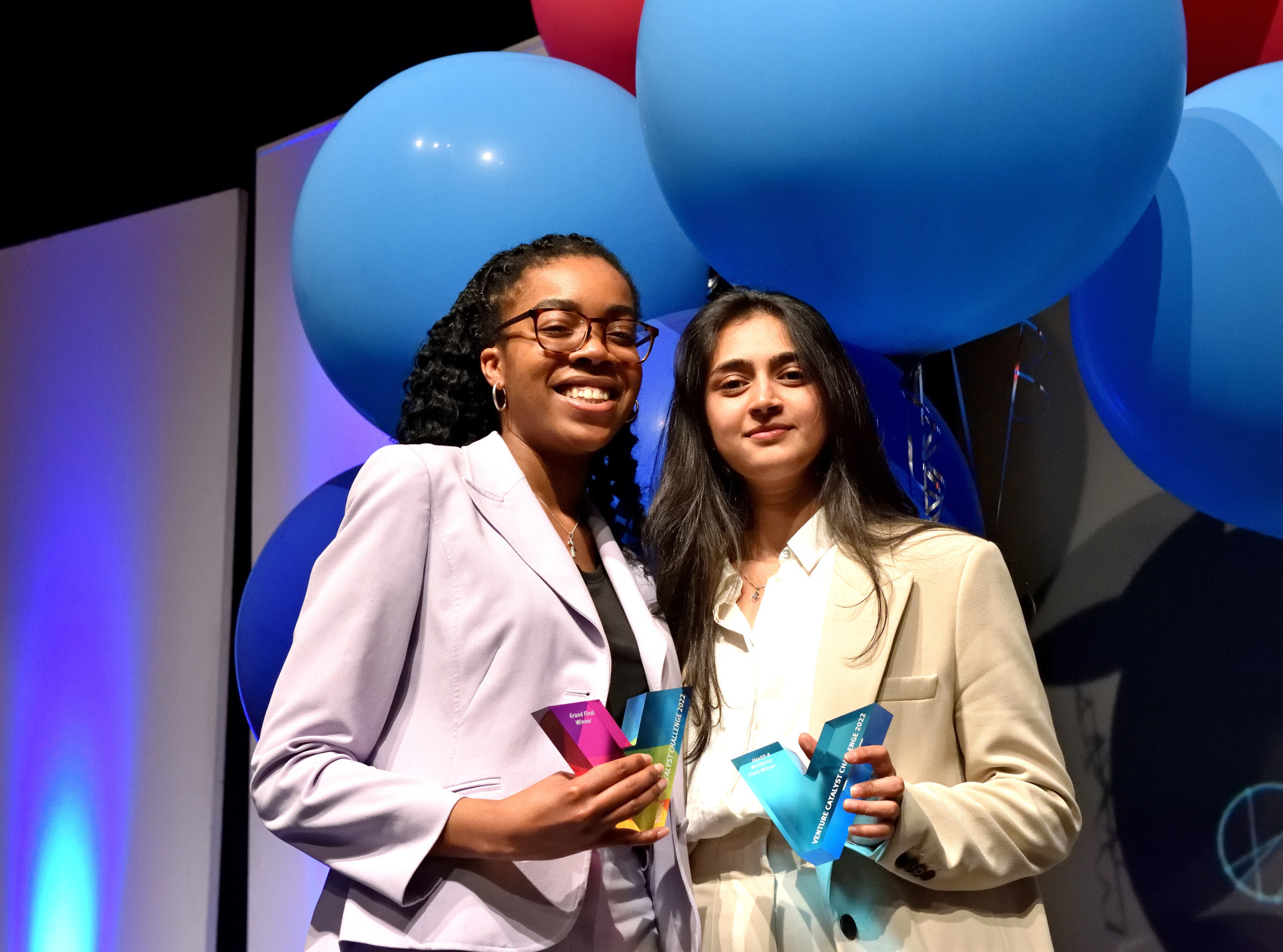 Two women smile holding trophies