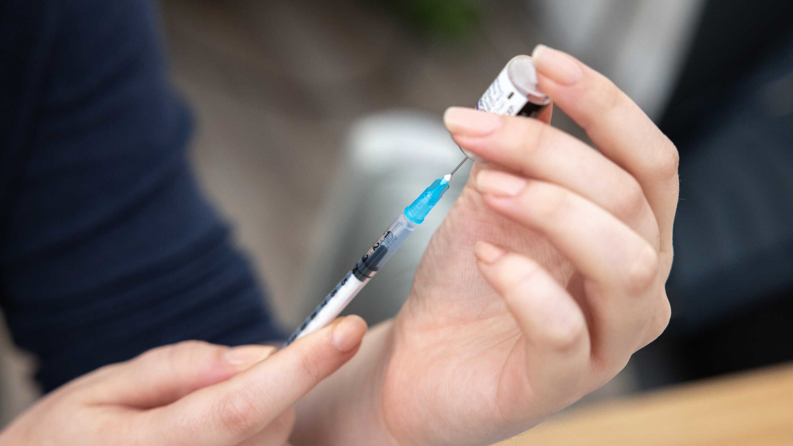 Photo of a hand holding a syringe and drawing out a vaccine from a vial.
