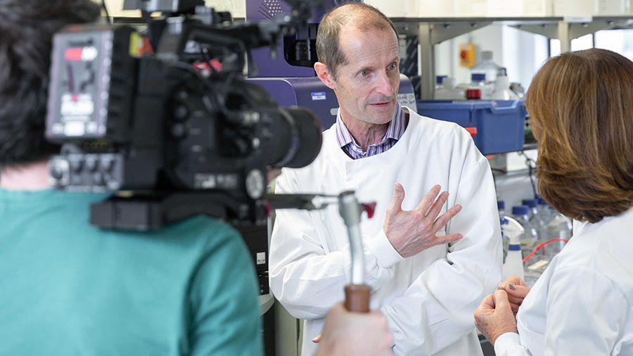 A photo of Professor Robin Shattock being filmed in a laboratory.