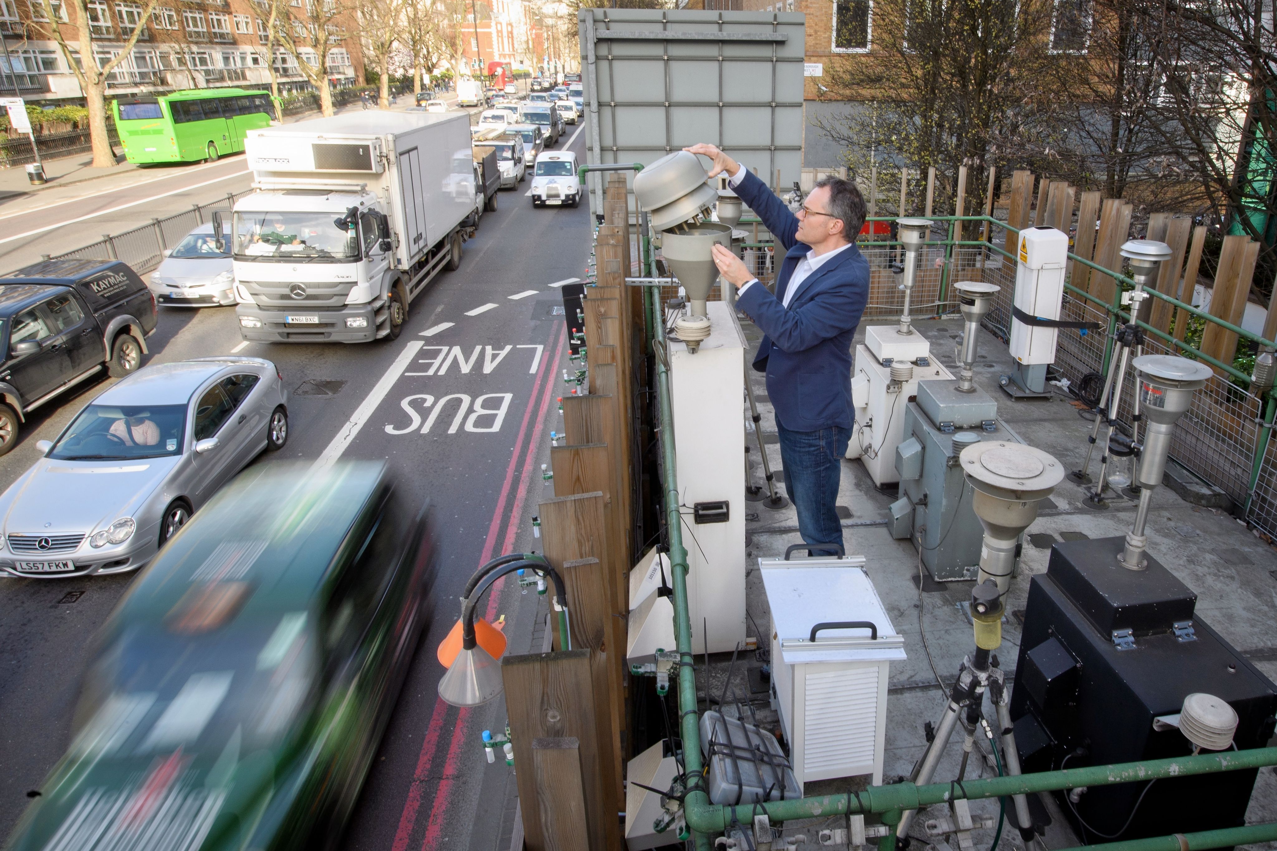Person inspecting a piece of equipment on a building roof above a busy London street