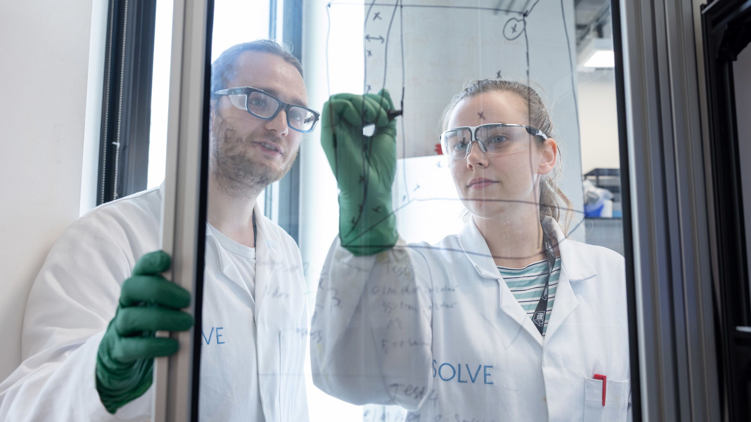 Two team members from SOLVE Chemistry writing on glass