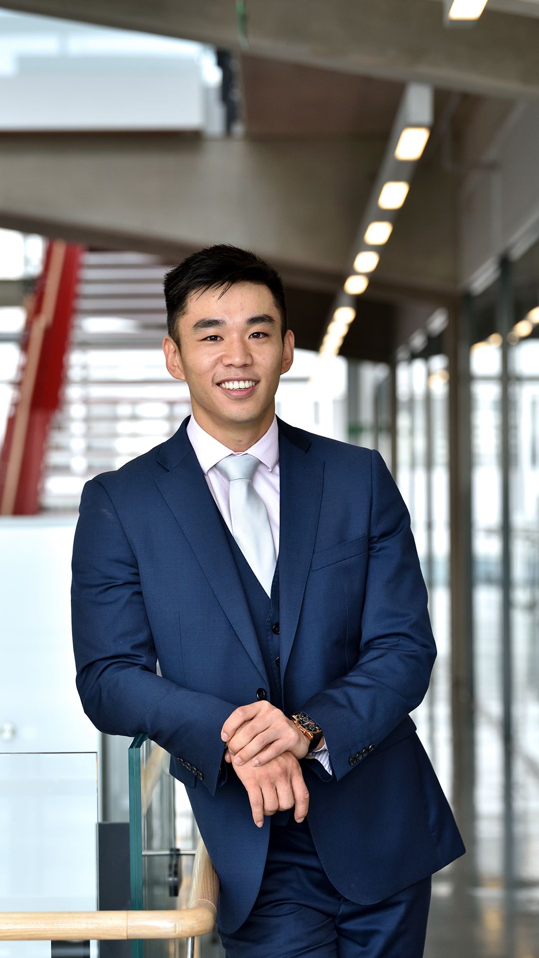 Brian is dressed in a suit leaning against the bannister of a staircase in Charing Cross Hospital