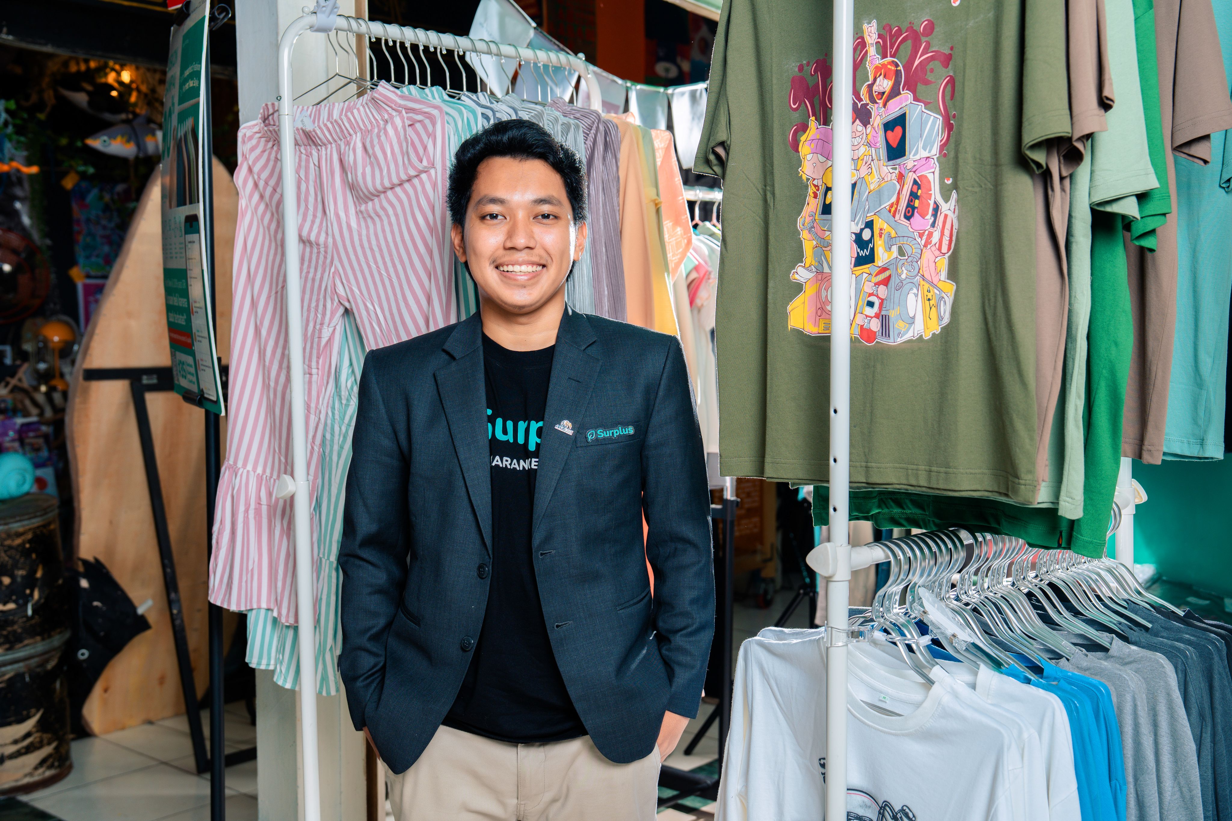 Agung stands smiling amongst clothes hung on rails