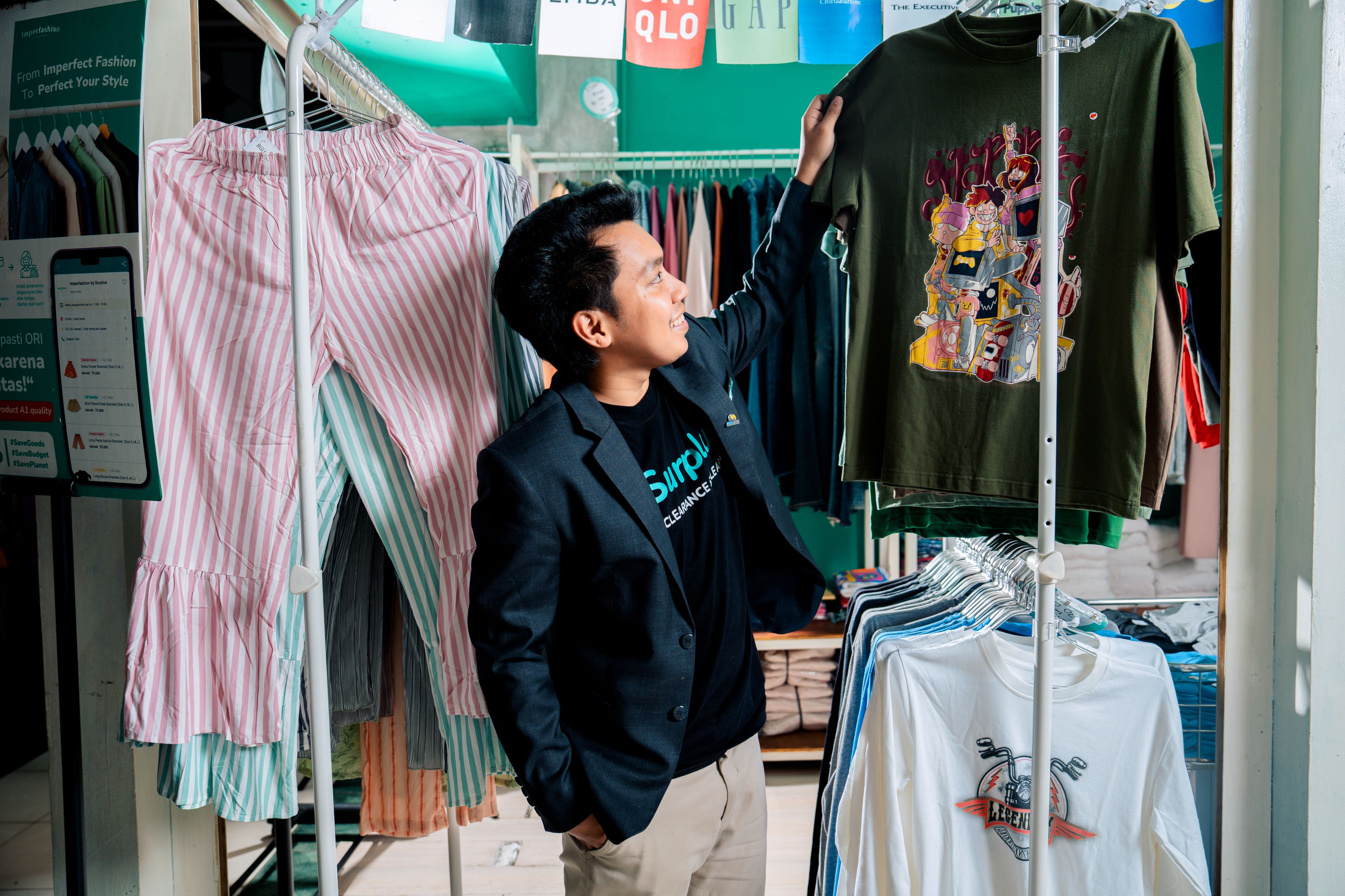 Agung stands smiling amongst clothes hung on rails