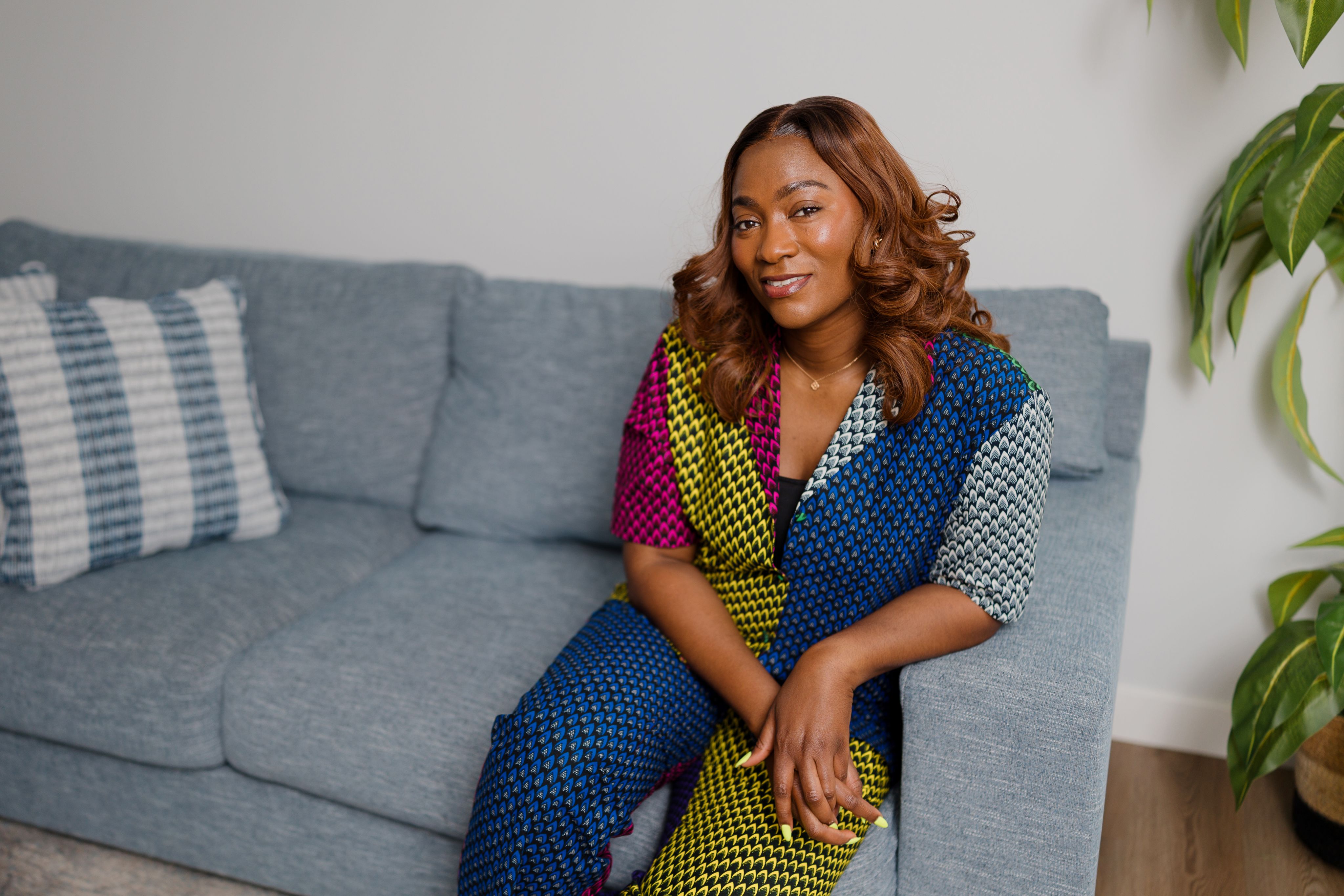 Jade Oyateru wearing a patterned top sat on a sofa next to a plant