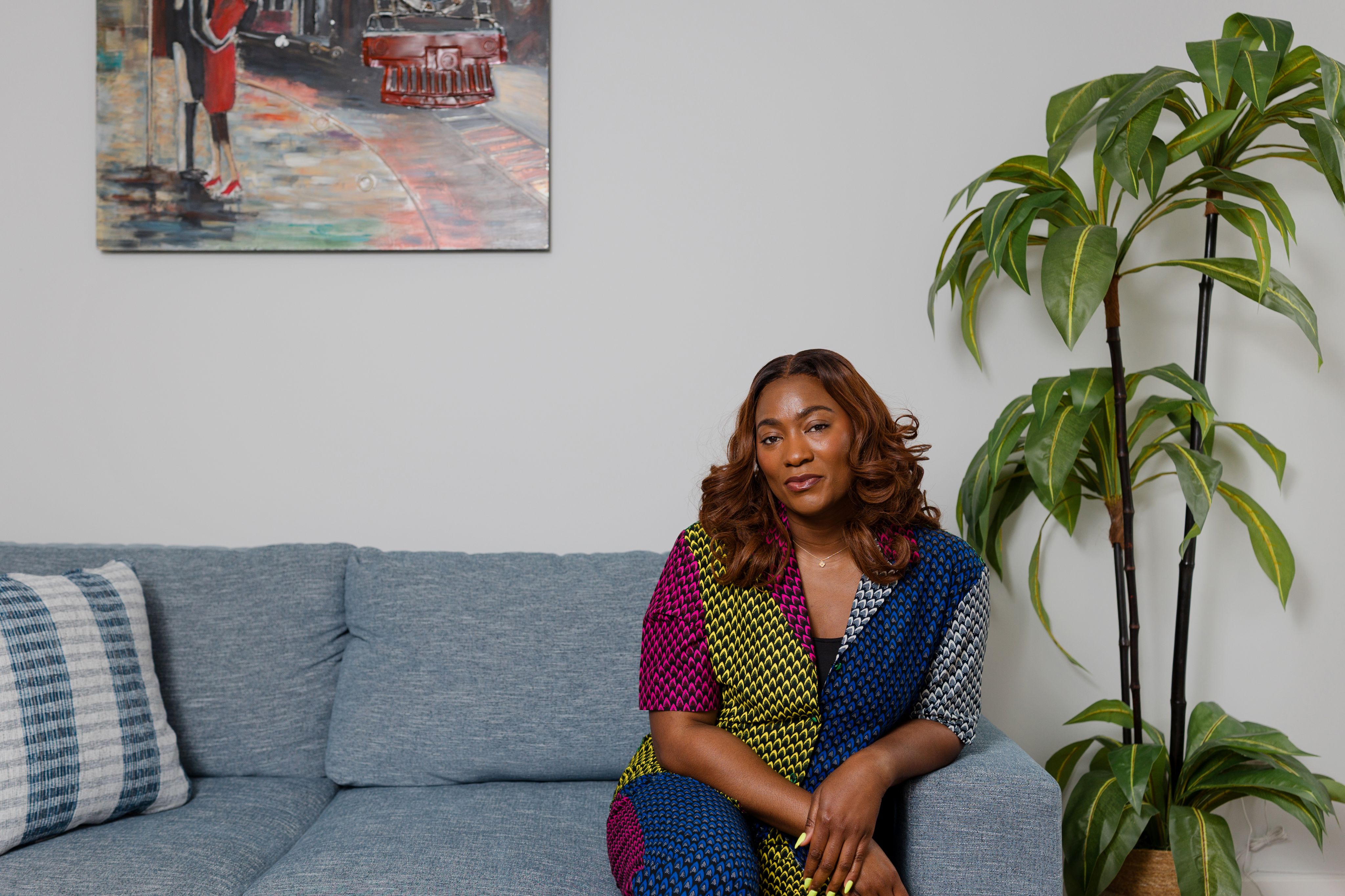 Jade Oyateru wearing a patterned top sat on a sofa next to a plant