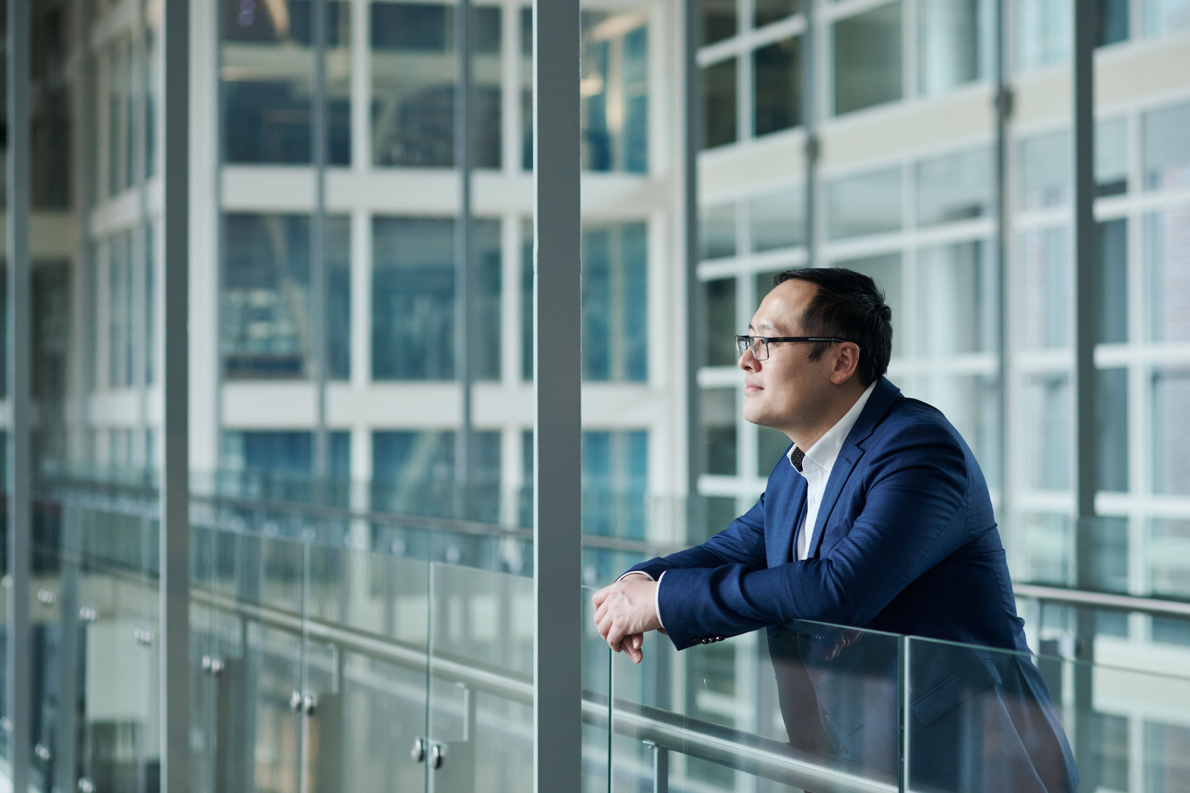 Dr Jiajun Cen stood indoors looking out of a window wearing a navy suit