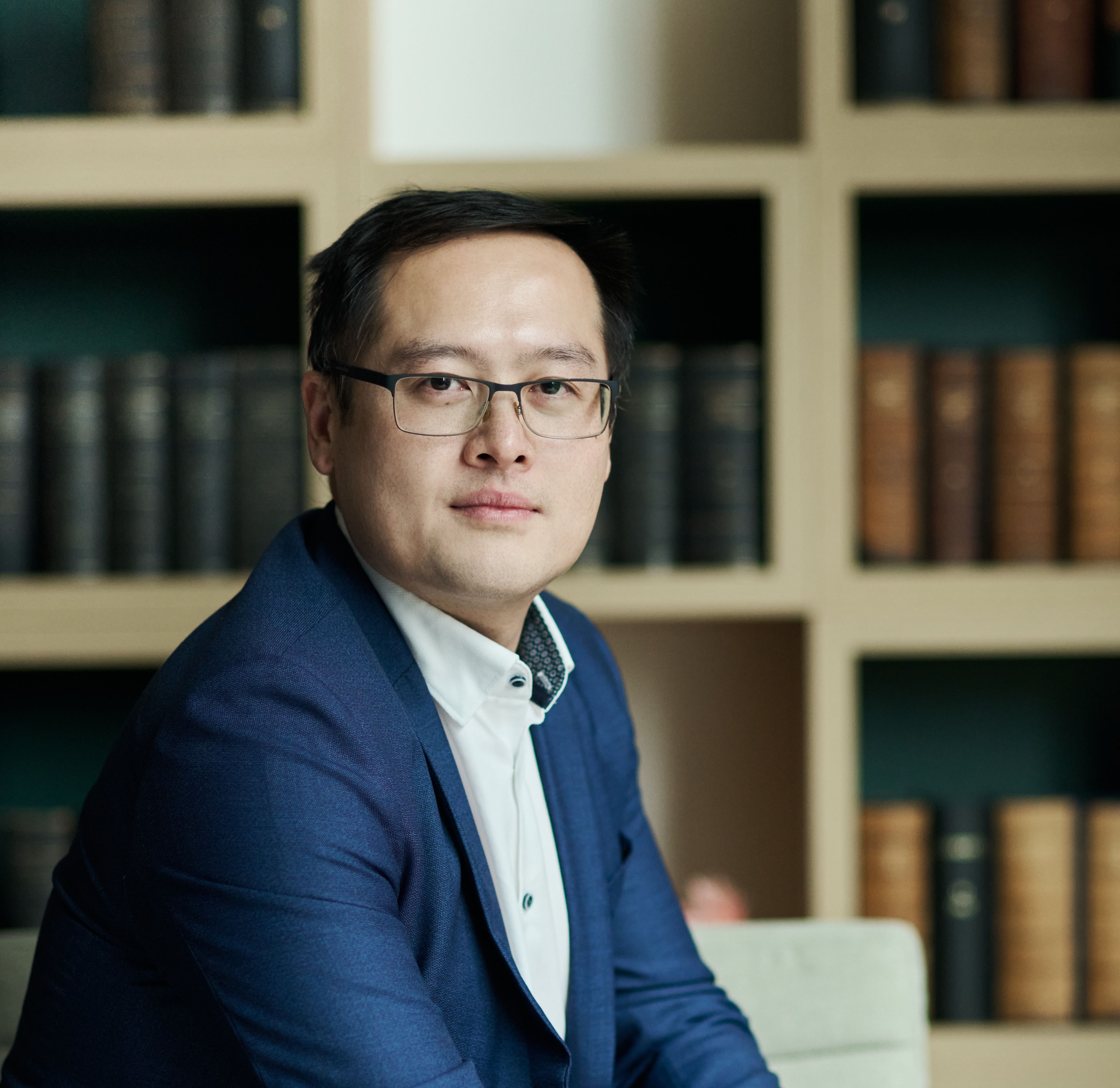 Dr Jiajun Cen sat indoors wearing a navy suit in front of a bookcase
