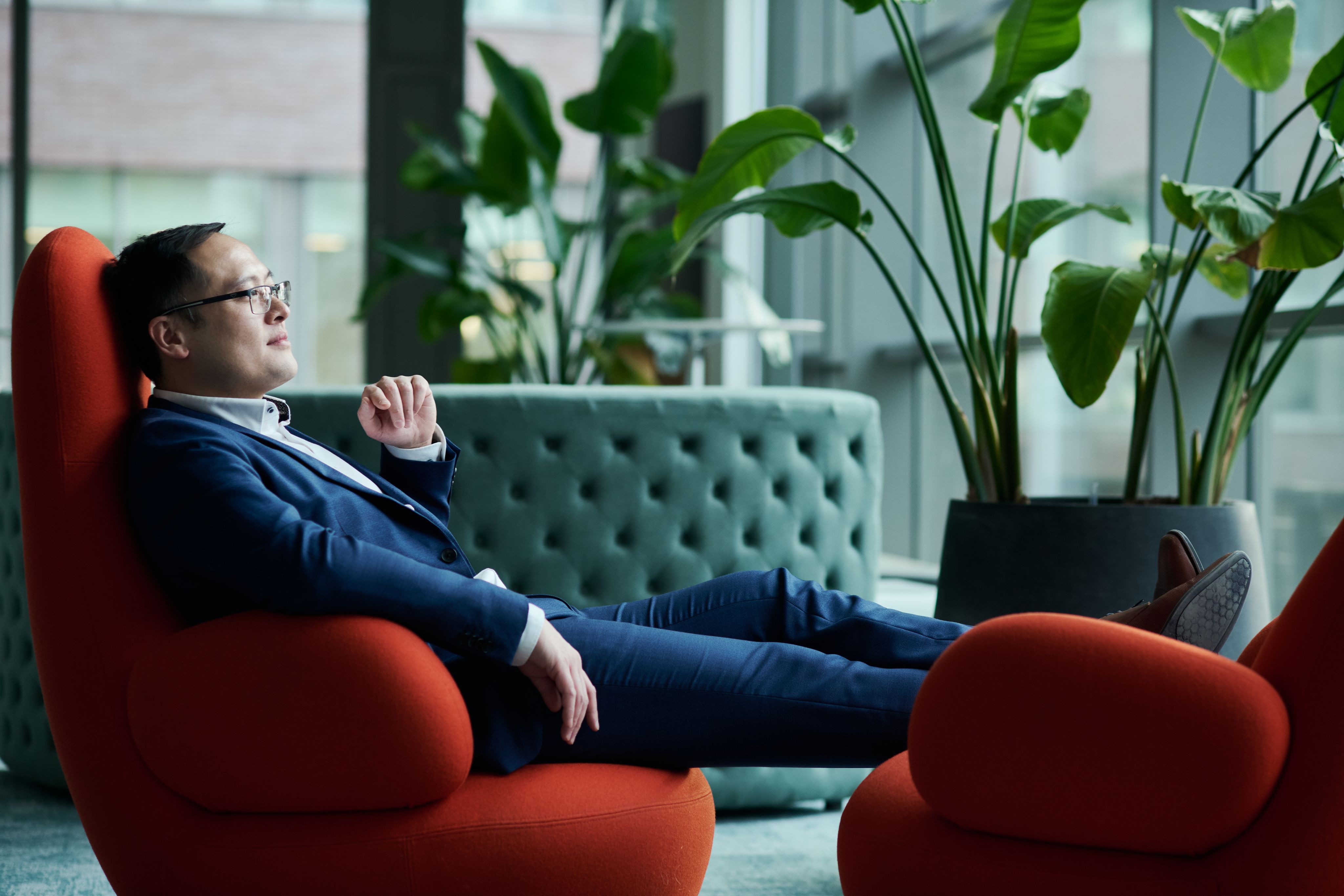 Dr Jiajun Cen sat on a red chair wearing a navy suit