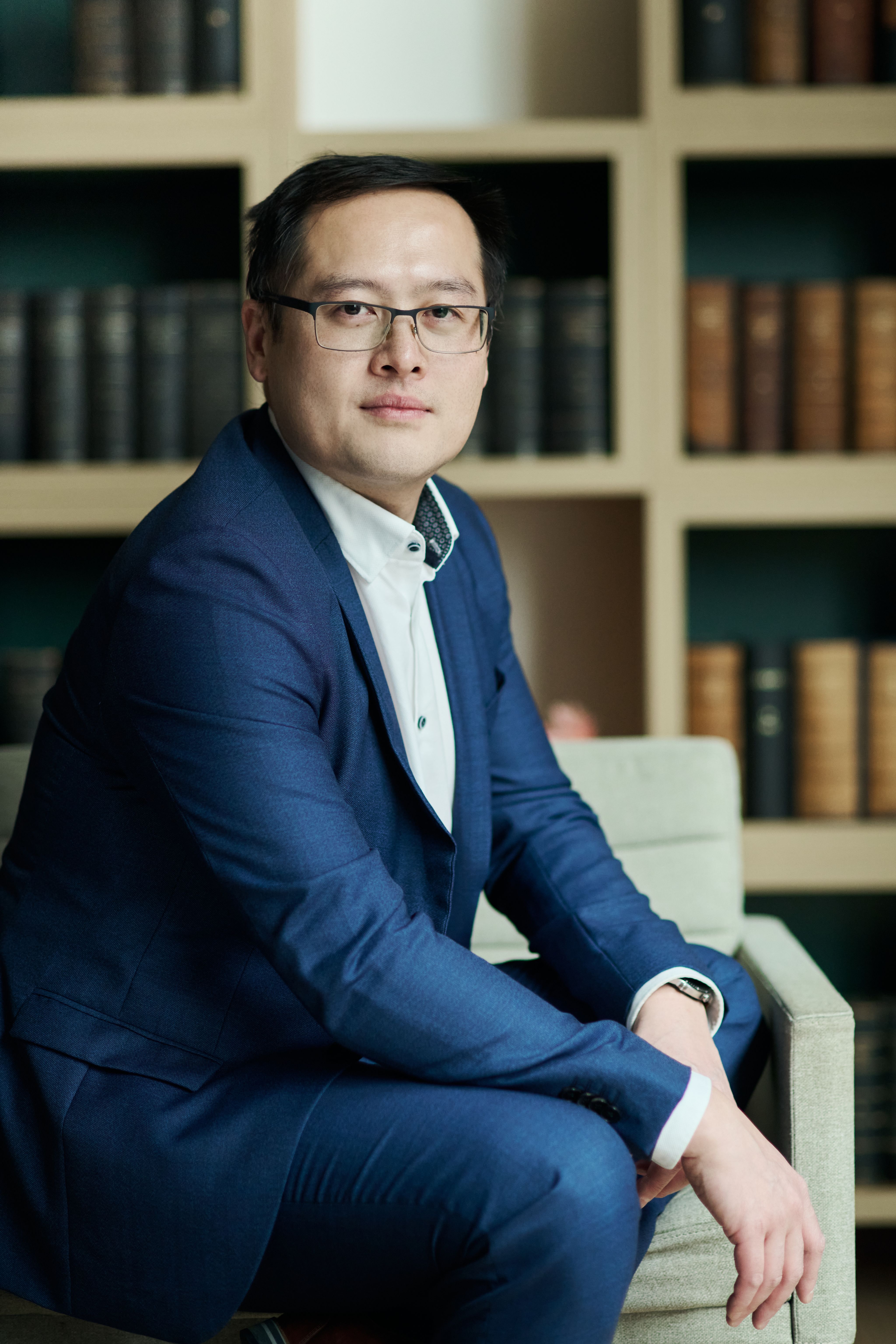 Dr Jiajun Cen sat indoors wearing a navy suit in front of a bookcase