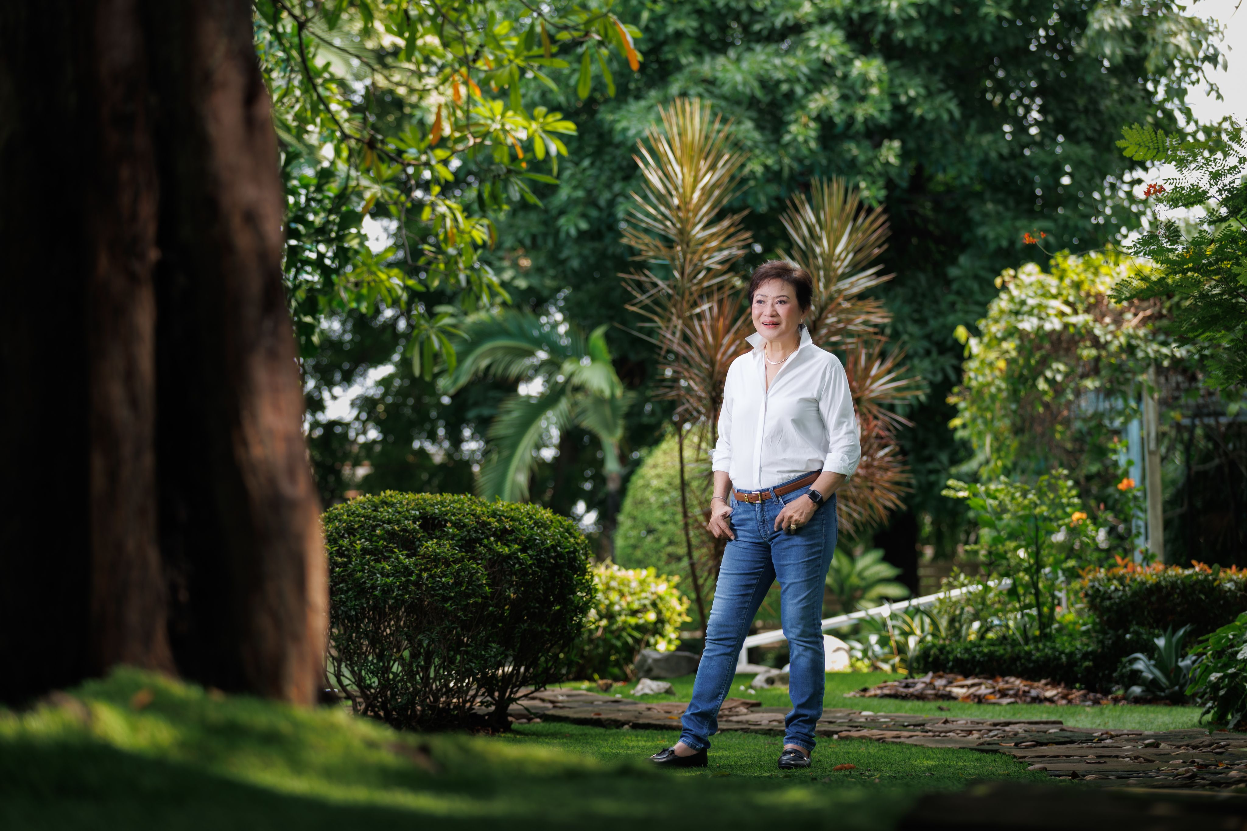 Kalaya Sophonpanich wearing a white shirt and jeans stood in some gardens