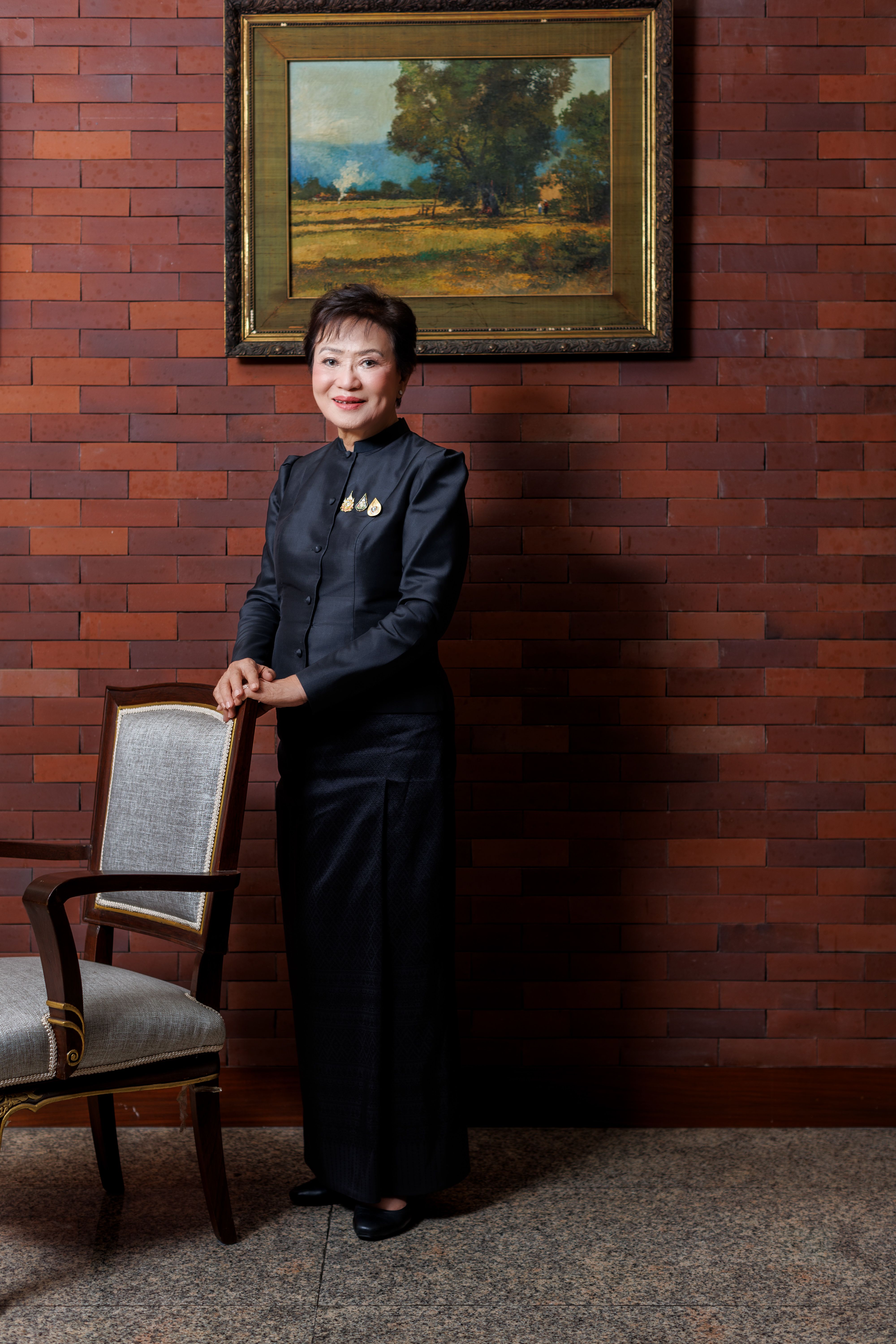 Kalaya Sophonpanich stood by a chair wearing dark clothes against a wall of terracotta metro tiles