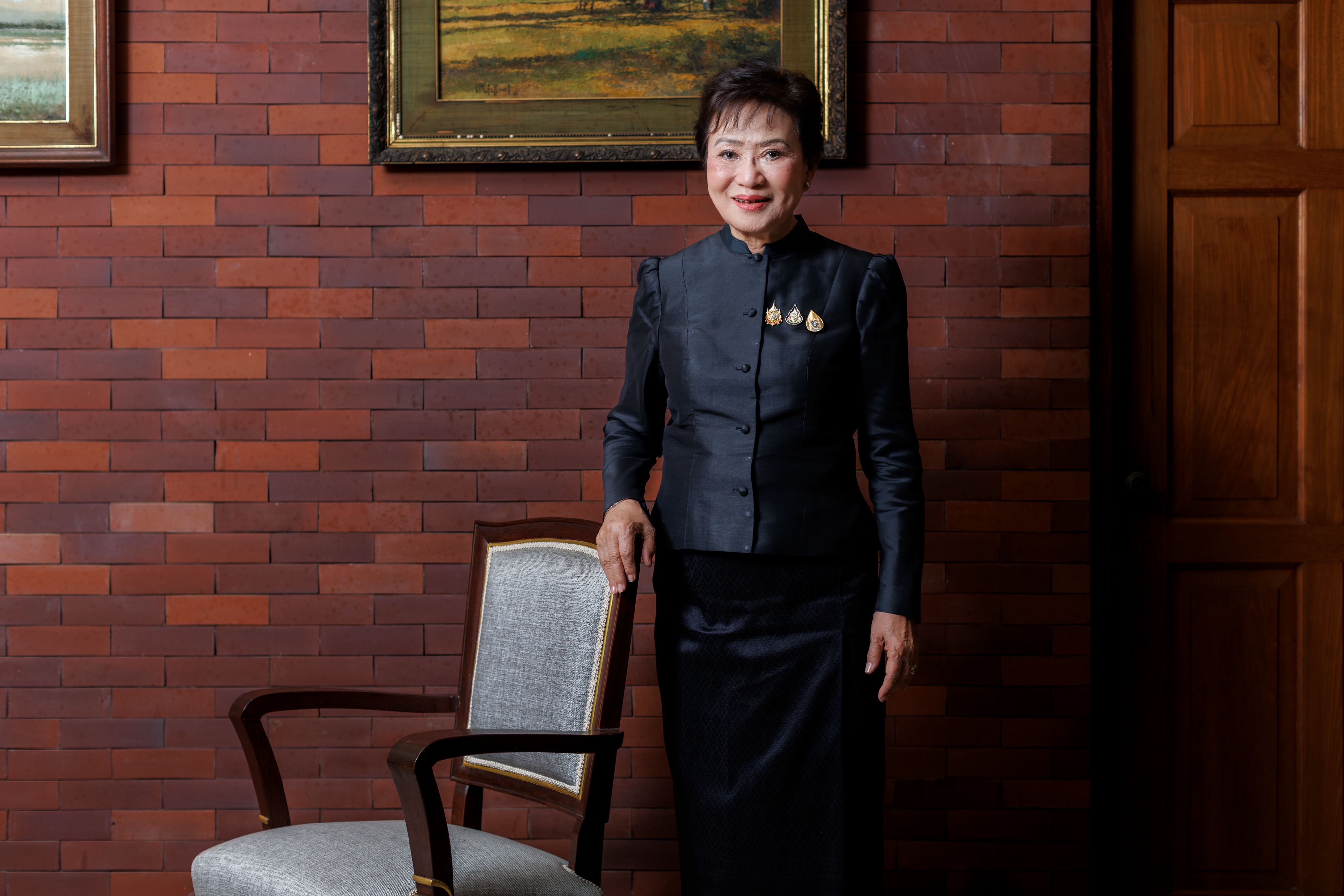 Kalaya Sophonpanich stood by a chair wearing dark clothes against a wall of terracotta metro tiles