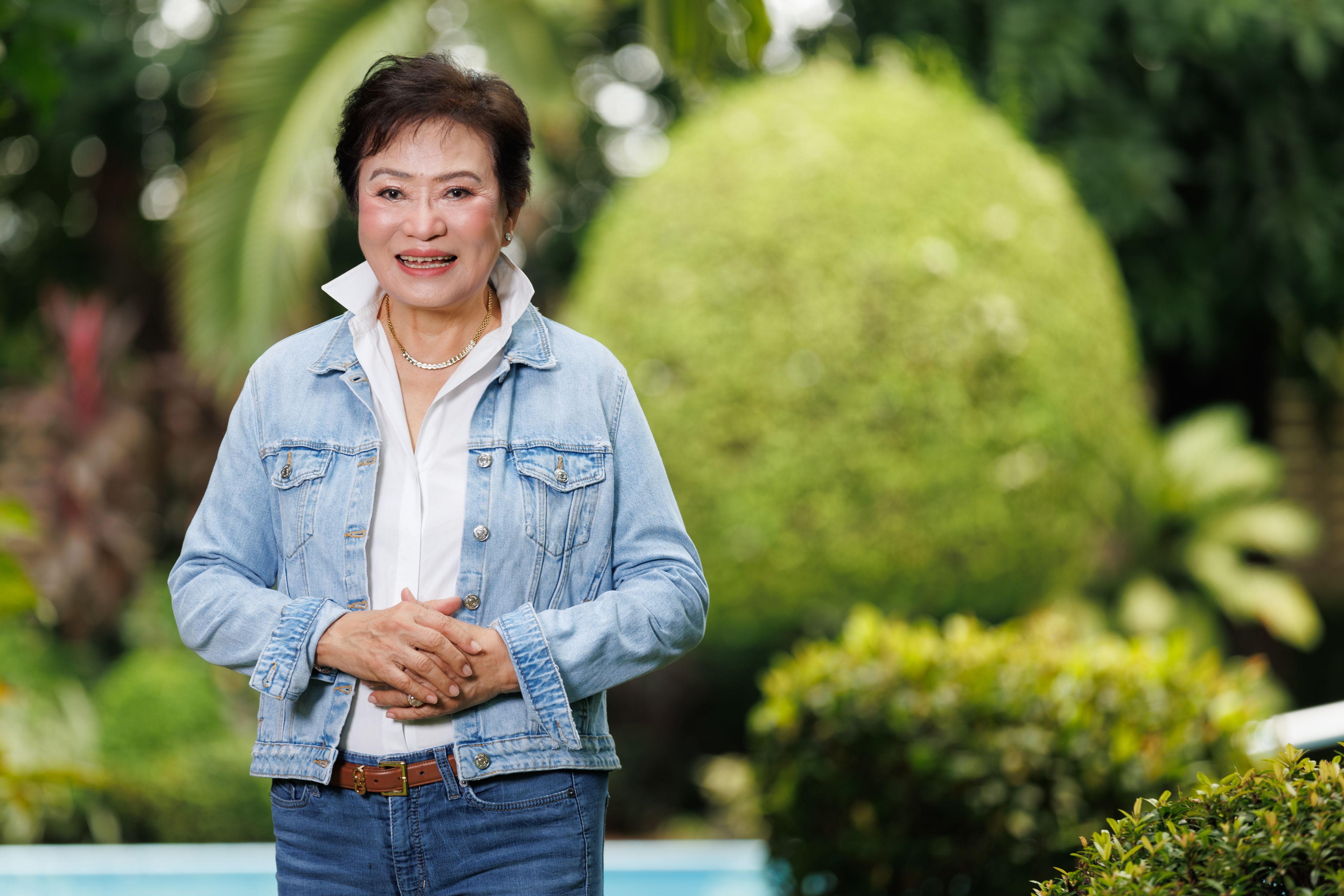 Kalaya Sophonpanich wearing a white shirt and jeans stood in some gardens