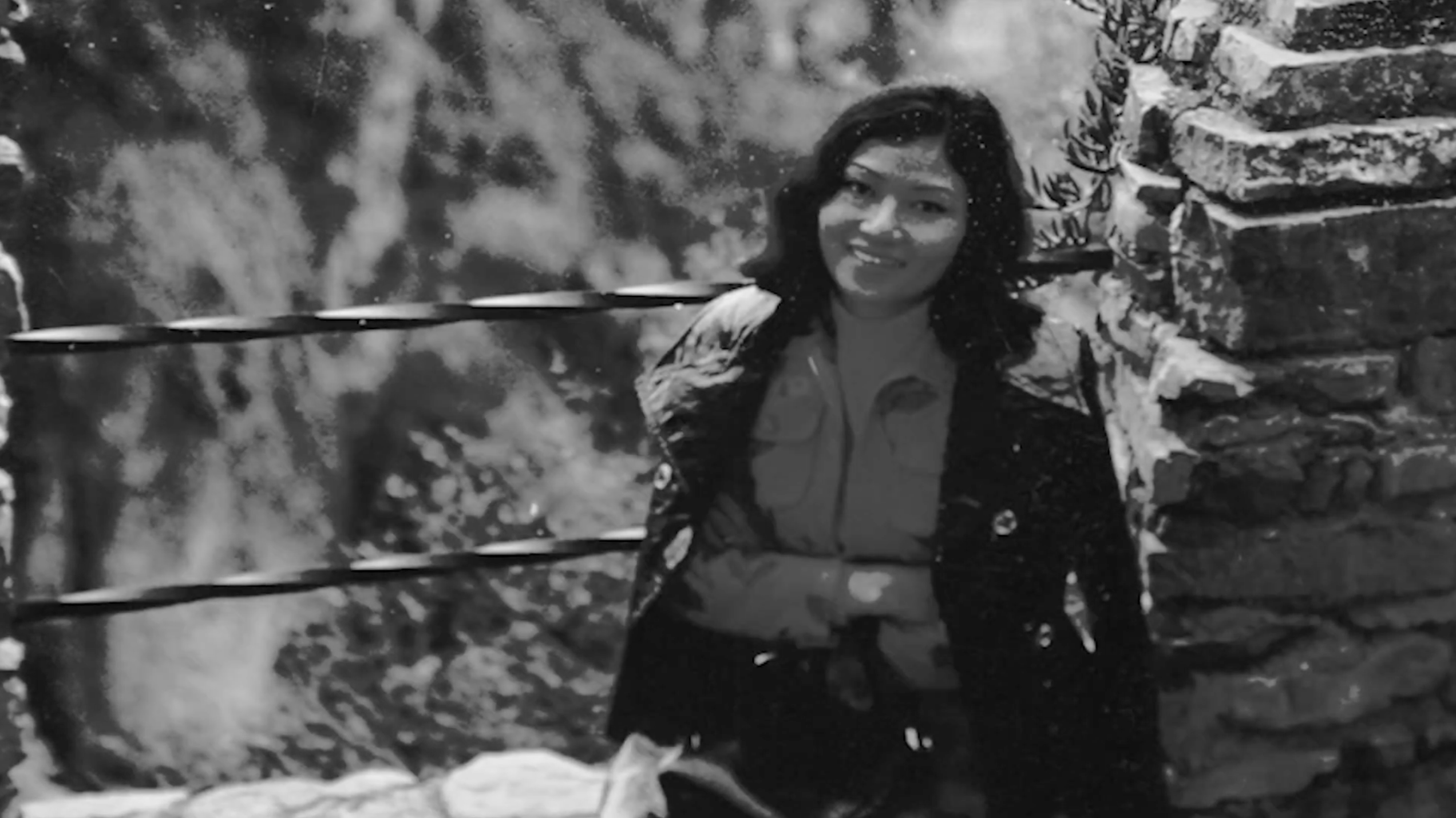 A black and white photo of a young Kalaya Sophonpanich sat on a wall smiling to camera