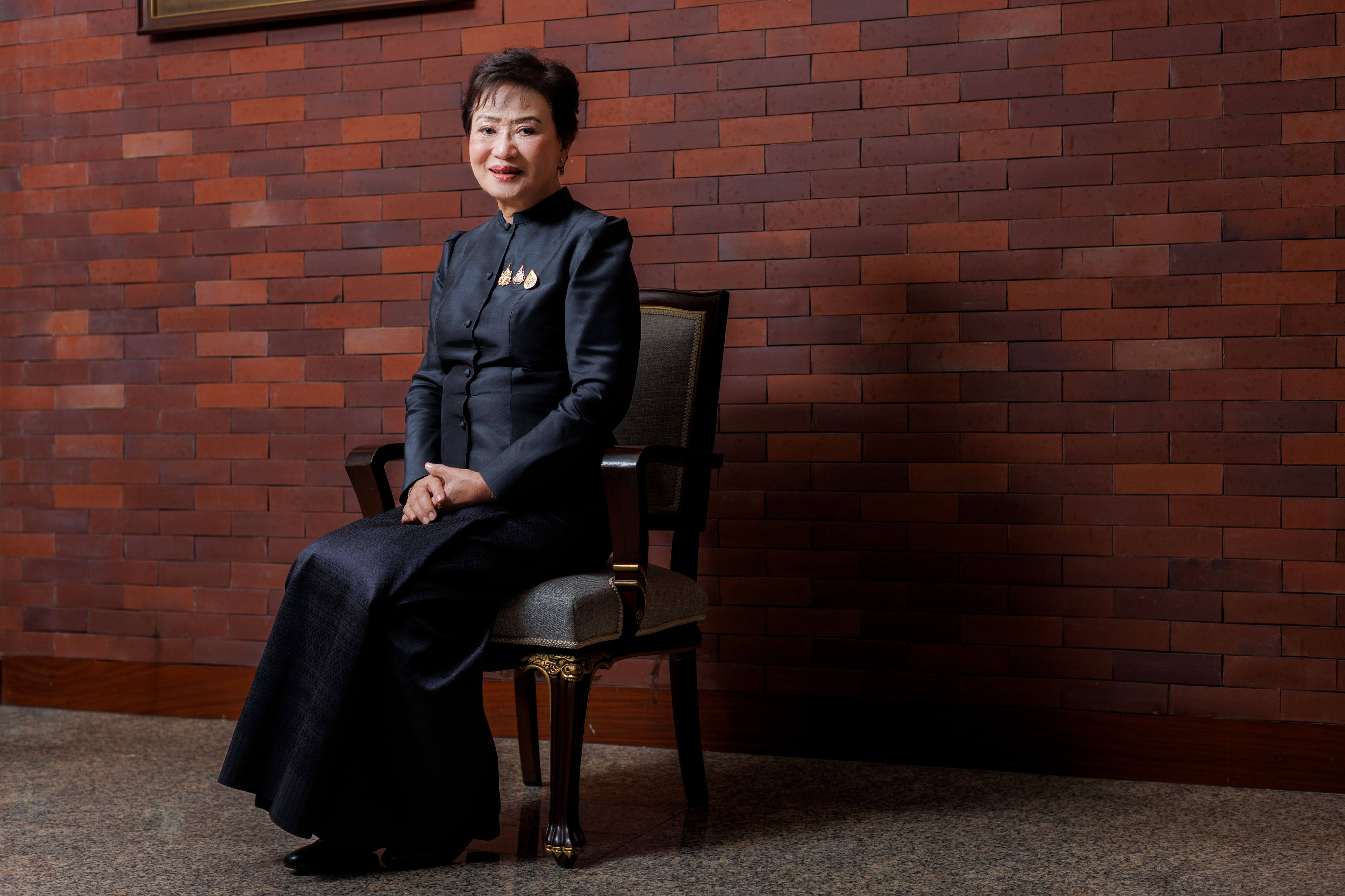 Kalaya Sophonpanich sat in a chair wearing dark clothes against a wall of terracotta metro tiles