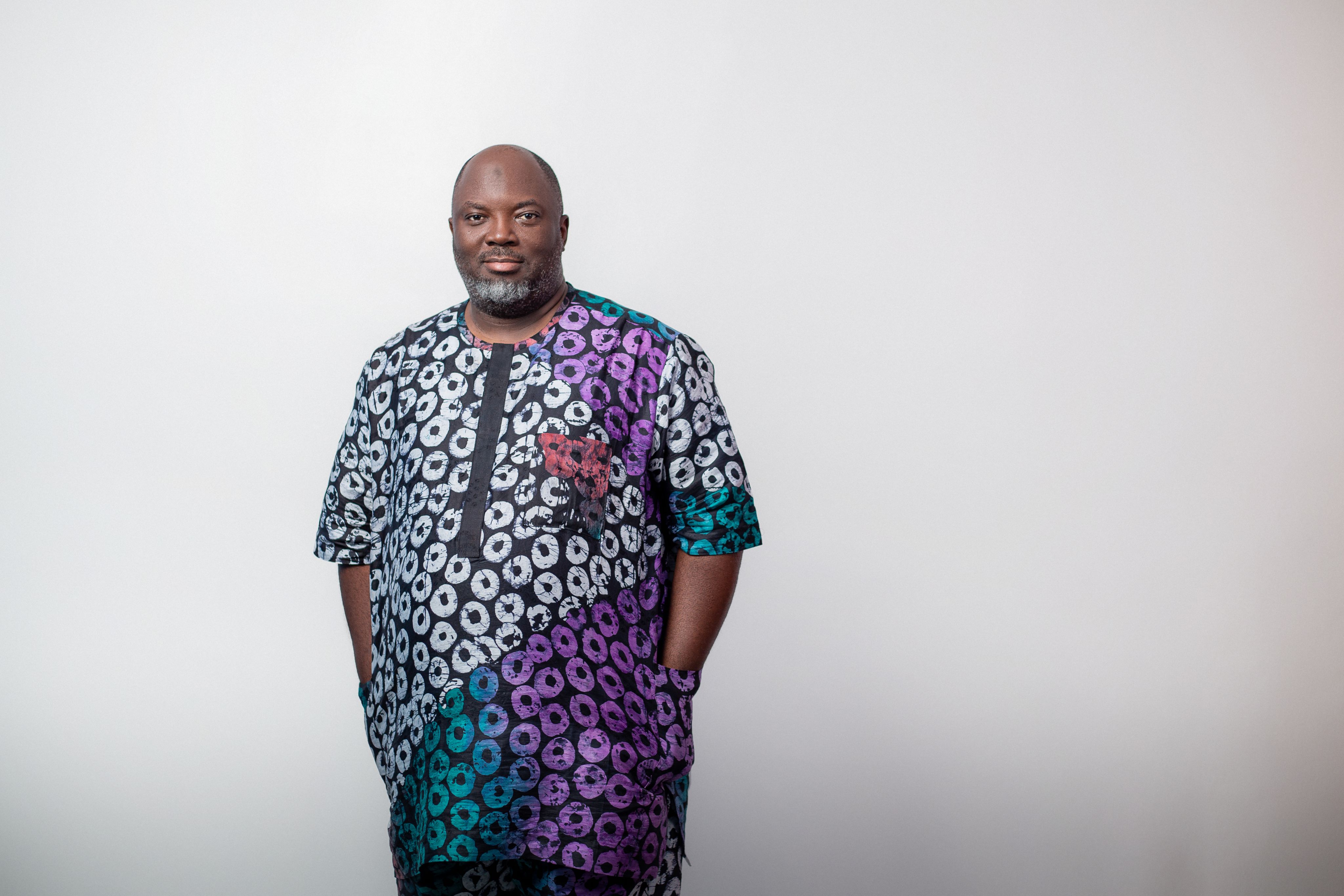 Kolawole Osinowo wearing a matching patterned Ankara short-sleeved top and trousers standing indoors by a window