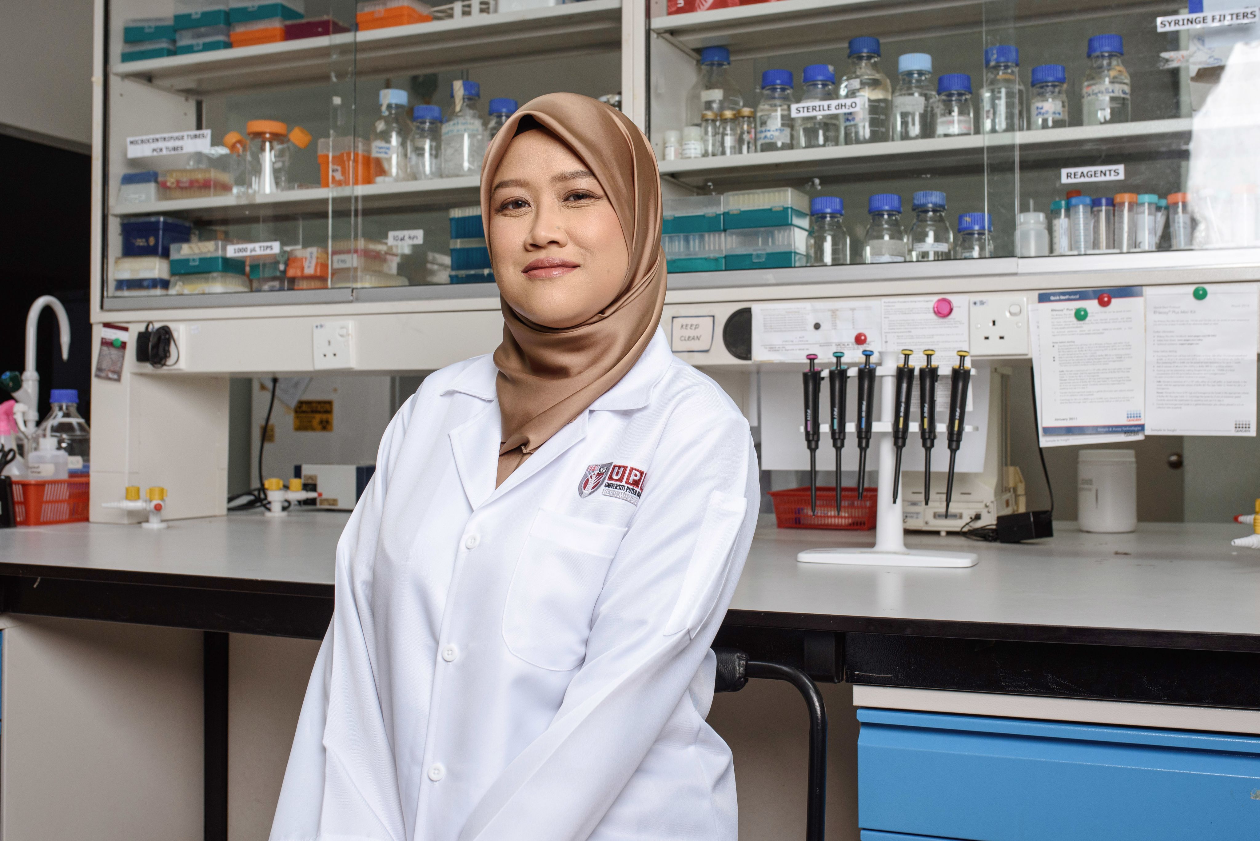Dr Mariatulqabtiah Abdul Razak in her lab wearing a lab coat gold headscarf