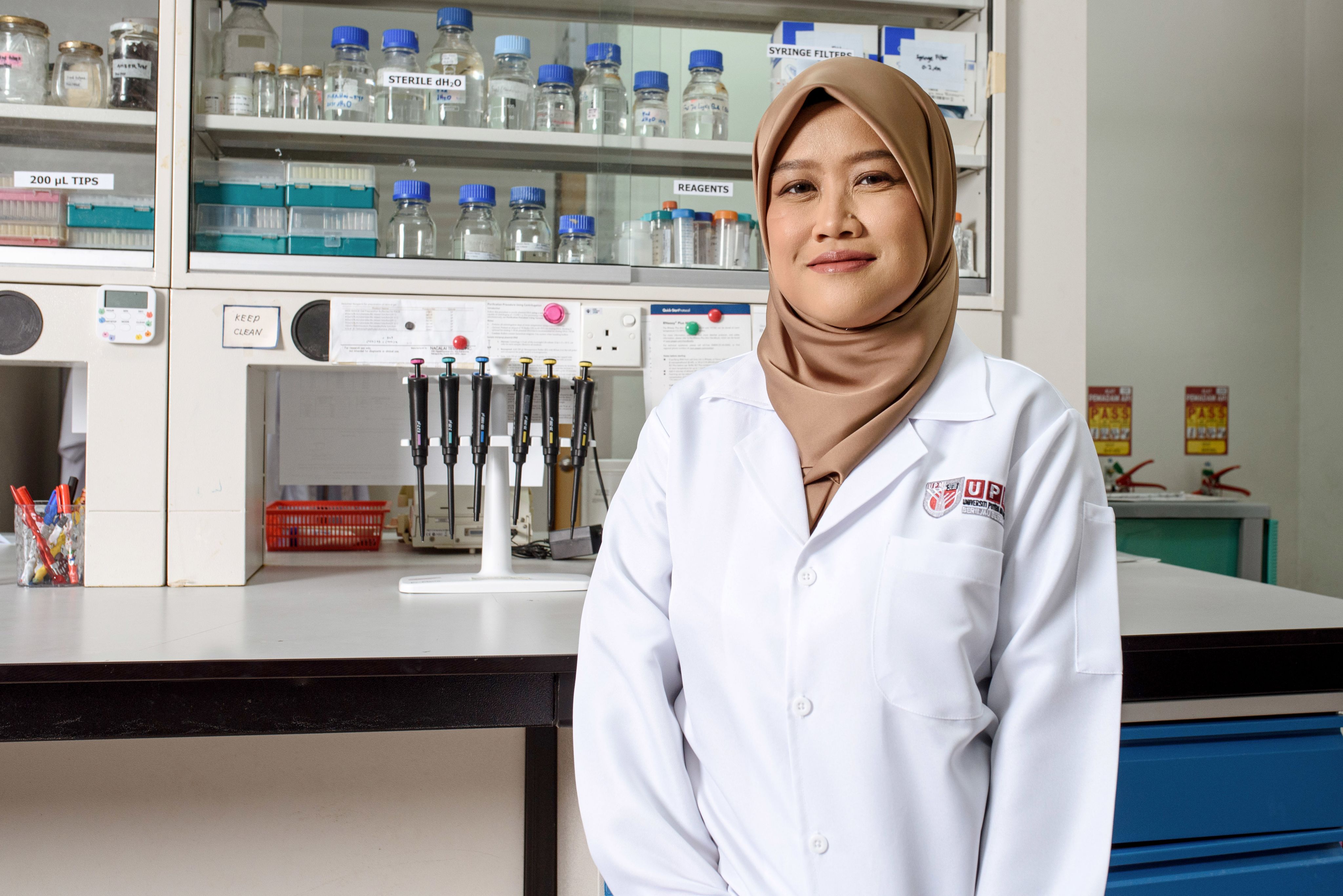 Dr Mariatulqabtiah Abdul Razak in her lab wearing a lab coat and a gold headscarf