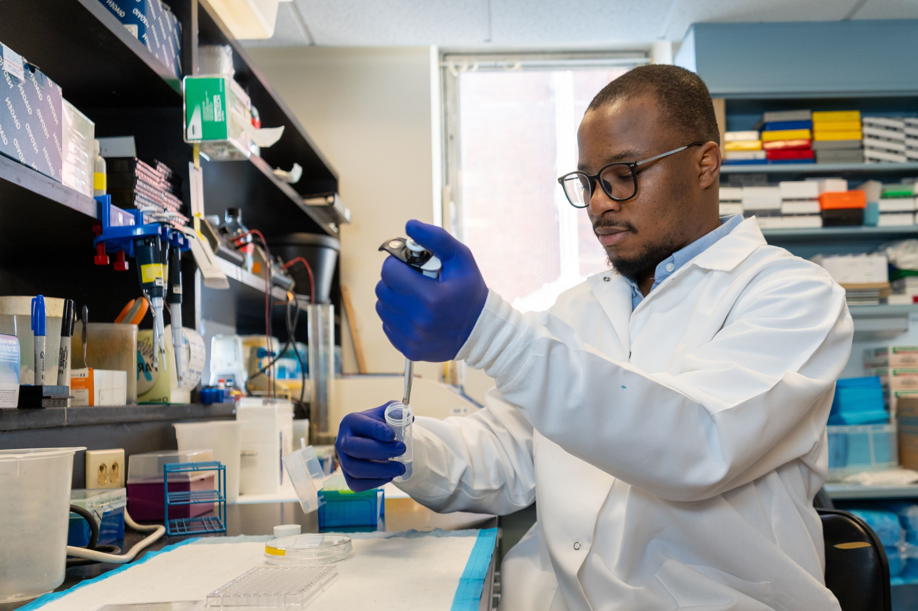 Tunde Oyebamiji in his lab wearing a lab coat and using a pipette